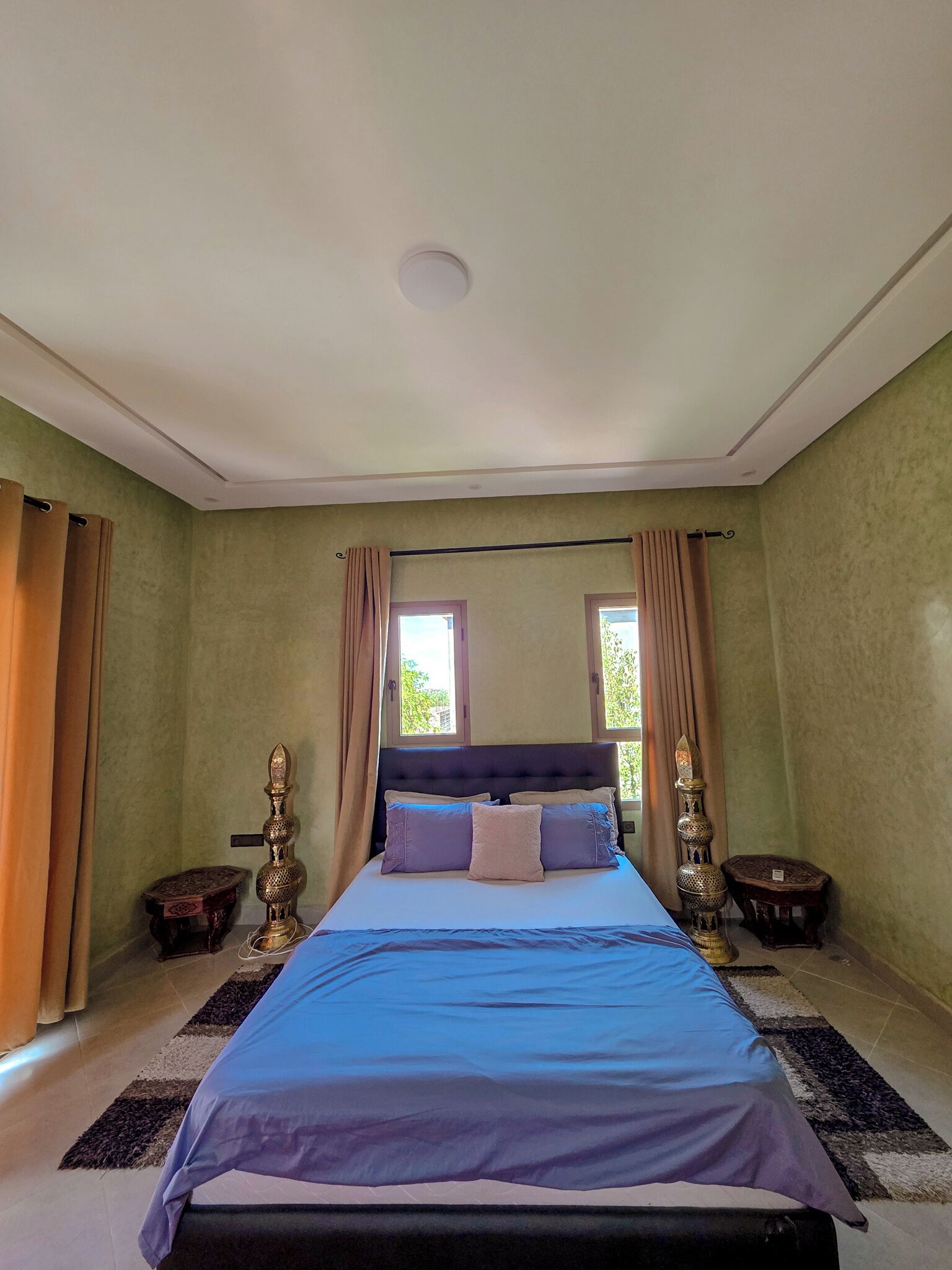 Ein Schlafzimmer mit einem Bett, zwei Fenstern, Vorhängen und Dekorationselementen.