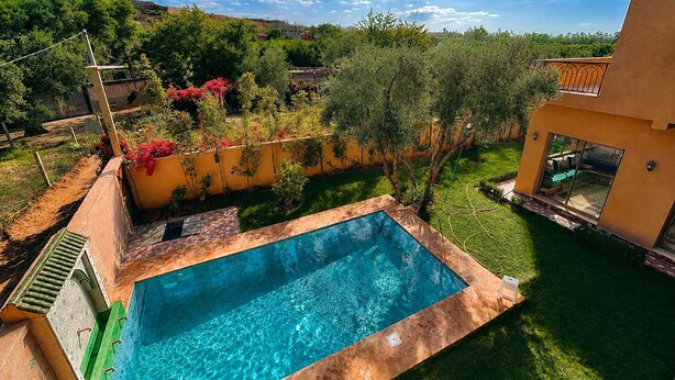 A swimming pool with a clear blue water, surrounded by a well-maintained lawn and a yellow wall. - Perfect 2-bedroom Villa with Pool in delightful Ourika (Ourika)