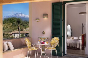 Un balcone con vista su una montagna, un tavolo con sedie e un letto con specchio e cuscini.