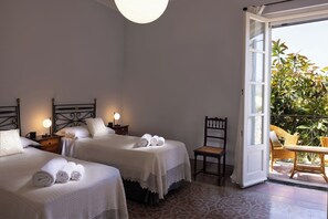 Camera d'albergo con due letti, una sedia, un tavolo e un balcone con piante.