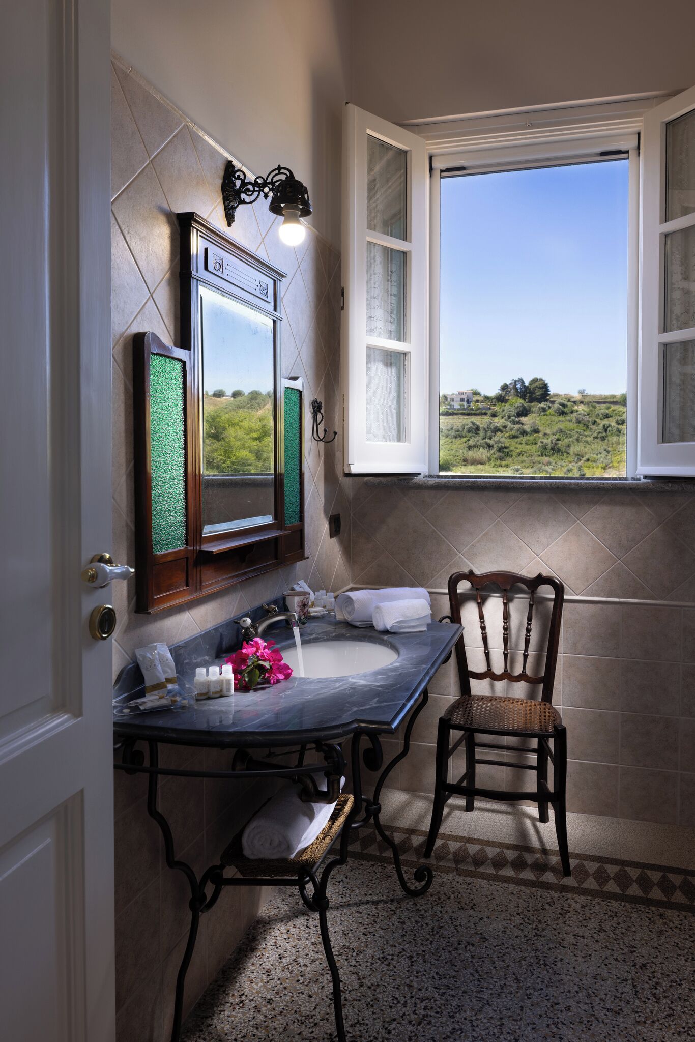 A bathroom with a bathtub, a window with a view, a mirror, and a chair.
