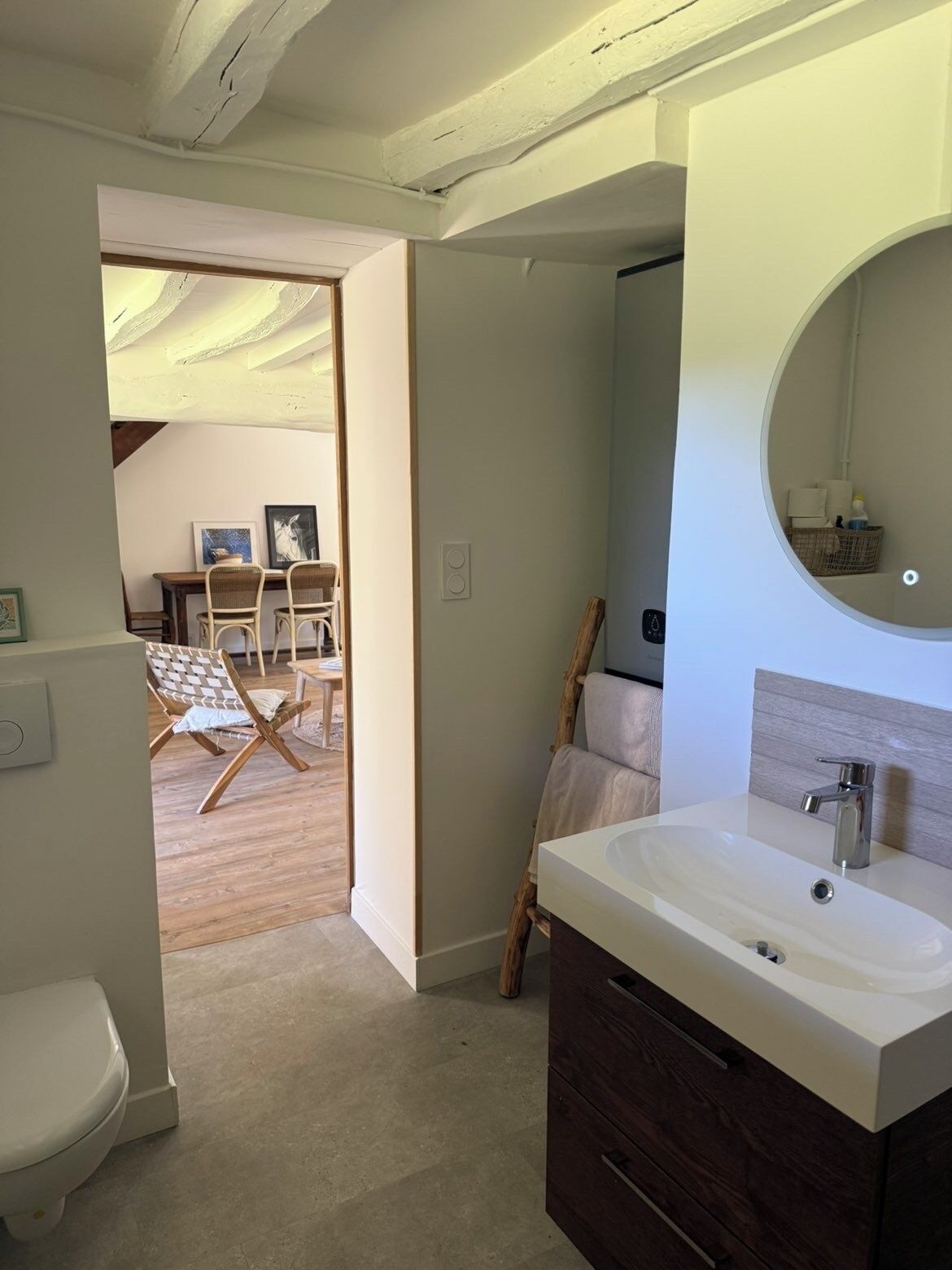 Un baño con un lavamanos blanco, un mueble de madera oscura y un espejo redondo.