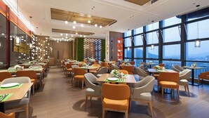 A modern restaurant with multiple dining tables and chairs, large windows with a city view, and a ceiling with recessed lighting. - Hampton by Hilton Huzhou Deqing (Huzhou)