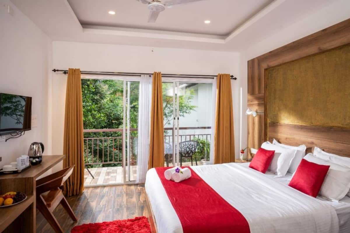 Habitación de hotel con cama, escritorio, televisor y balcón con cortinas.