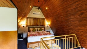 Un dormitorio con techo inclinado, paredes de madera, una cama con cubrecama blanco, dos lámparas de pared y un ventilador de techo.