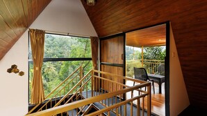 Un interior de madera con una escalera que conduce a un balcón con vistas a un bosque.
