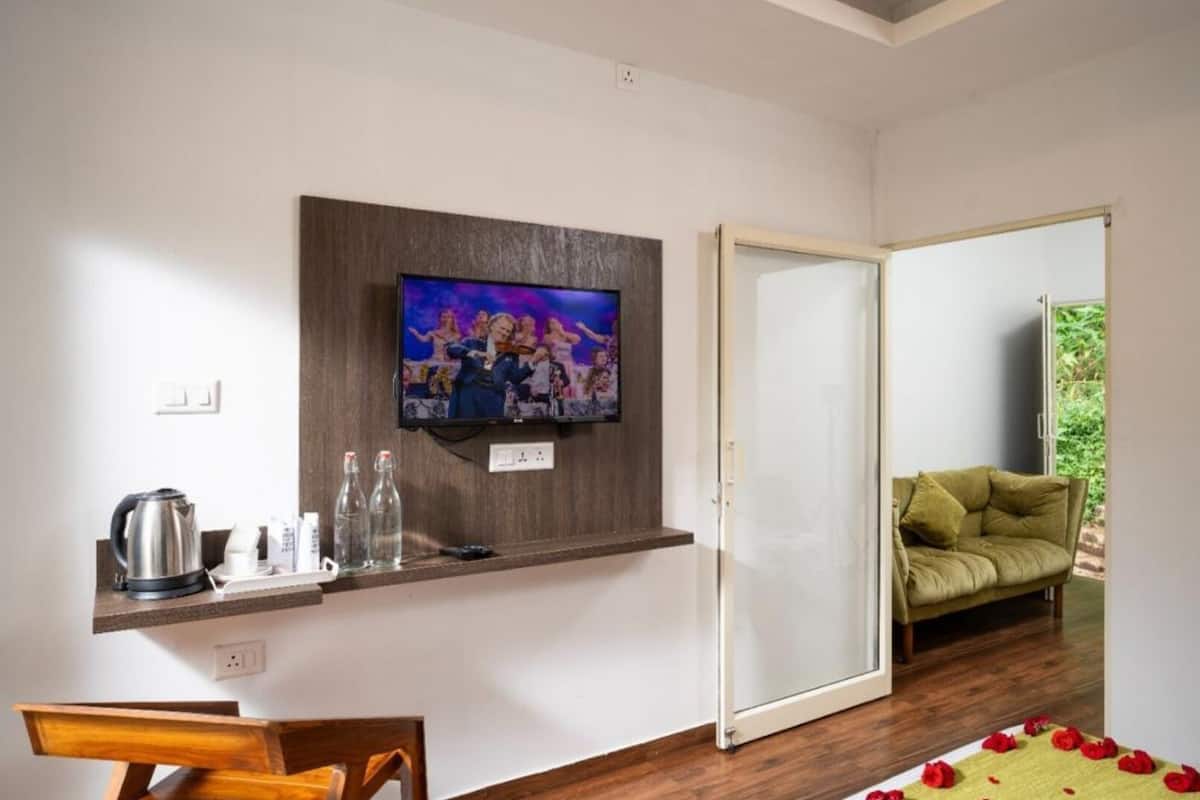 Una habitación con una televisión instalada en la pared, un banco de madera, un sofá y una puerta corredera que da a un espacio al aire libre.