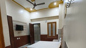 A bedroom with a bed, a chair, a television, a wardrobe, and a ceiling fan. - Gopal Dham (Mathura)
