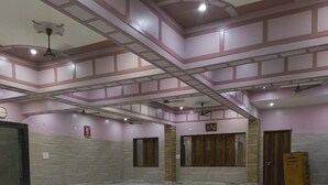 A spacious hall with a marble floor, ceiling fans, and a clock on the wall. - Gopal Dham (Mathura)
