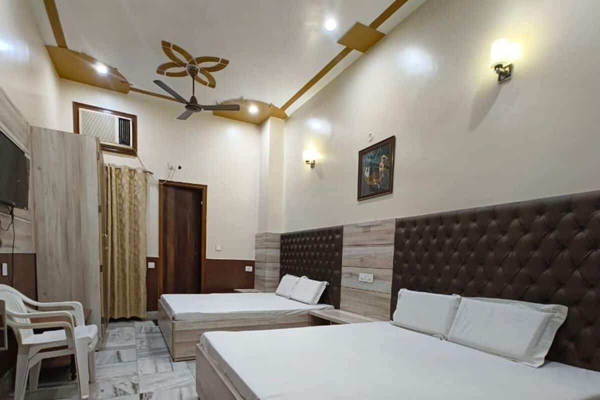 Habitación de hotel con dos camas, ventilador de techo, una lámpara en la pared y un cuadro.