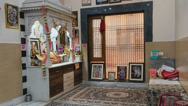A room with a prayer area, a large window with bars, and a patterned carpet. - Gopal Dham (Mathura)