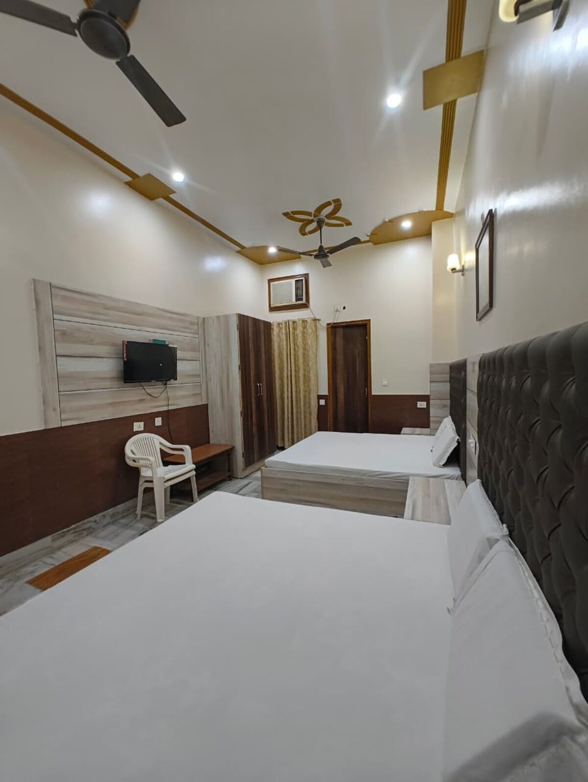A hotel room with two beds, a TV, ceiling fans, and a small seating area.