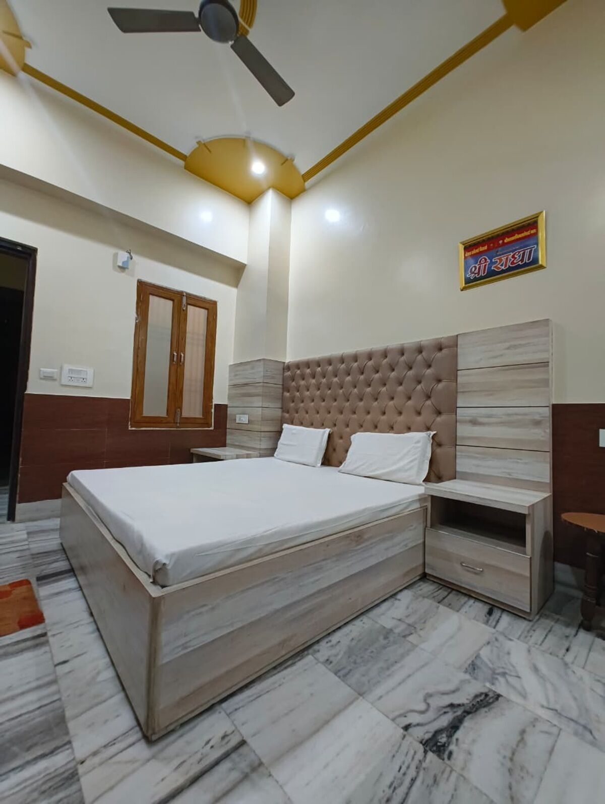 A bedroom with a bed, a ceiling fan, a nightstand, and a wall-mounted shelf.