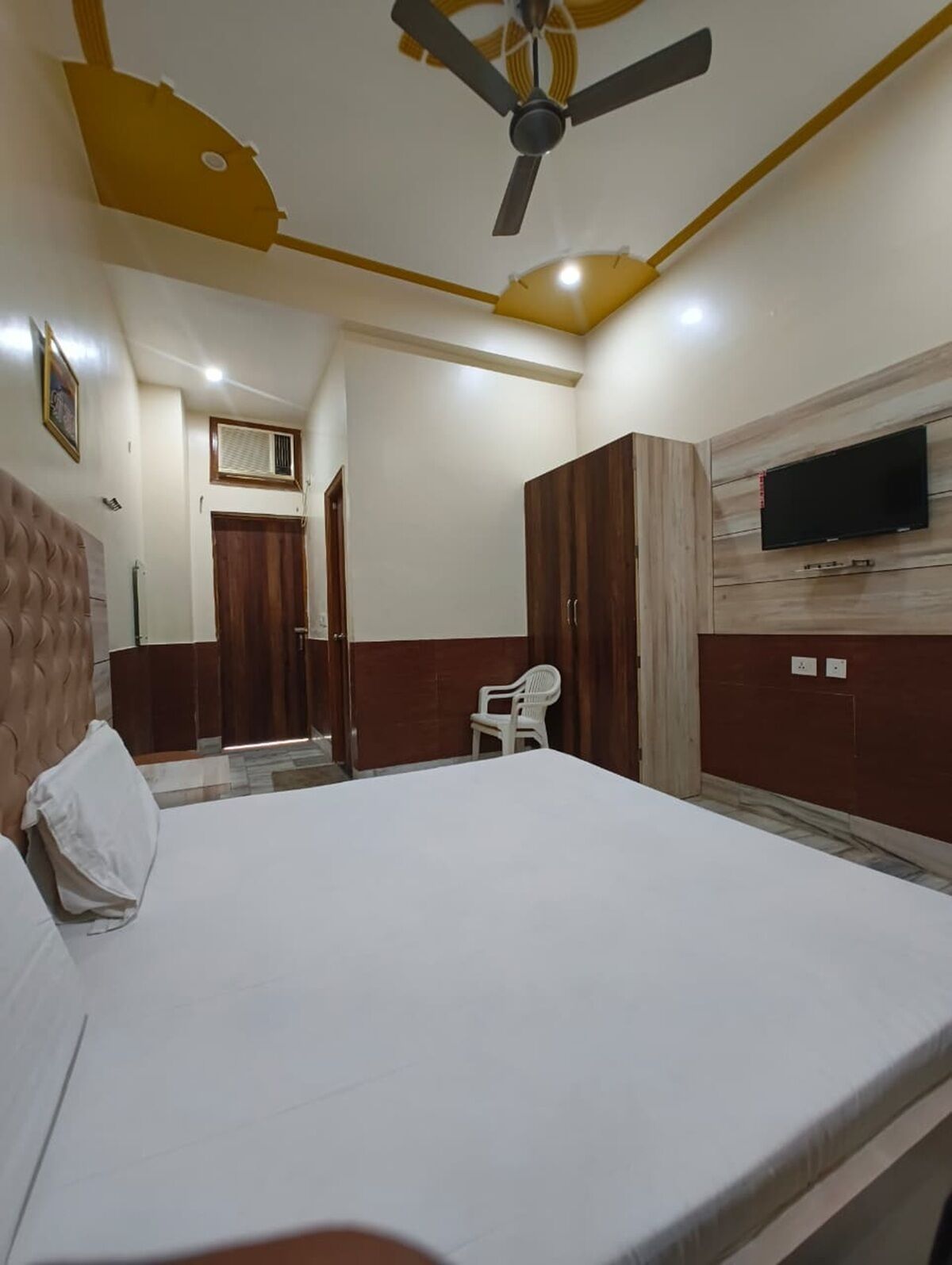 A bedroom with a bed, a ceiling fan, a TV mounted on the wall, and a wardrobe.