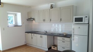 Una cocina con gabinetes blancos, encimera negra, microondas y refrigerador.