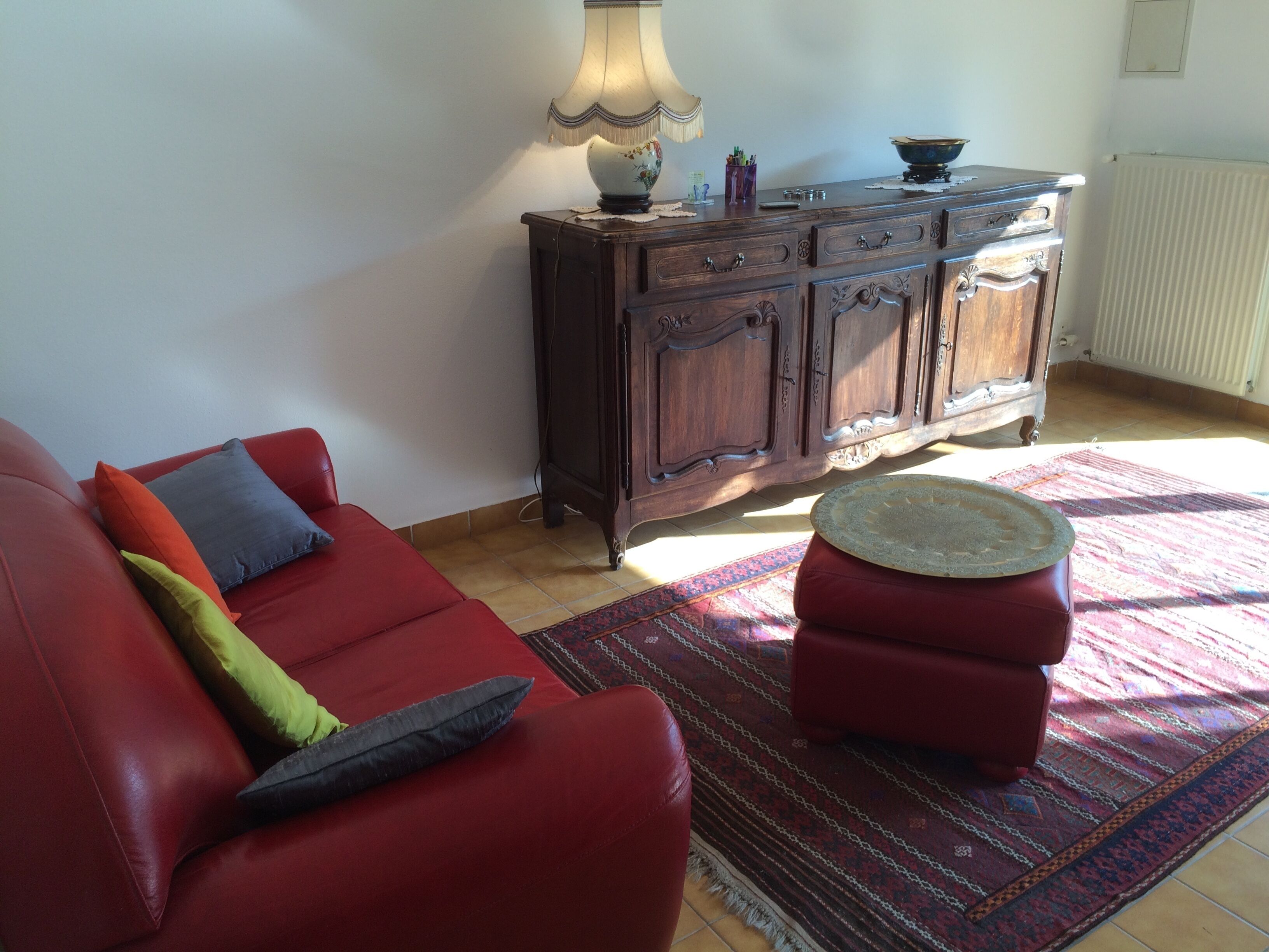 A living room with a red sofa, a wooden cabinet, and a patterned rug.