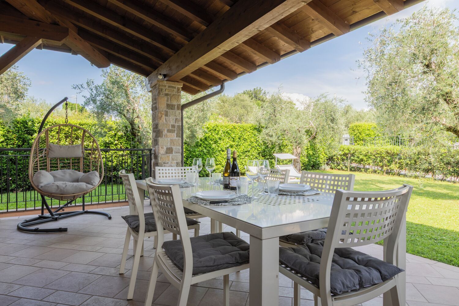 An outdoor patio with a table set for dining, surrounded by chairs with cushions.