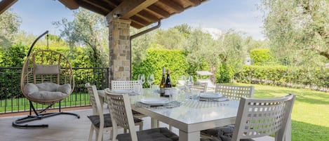 Une terrasse extérieure avec une table dressée pour le repas, entourée de chaises dotées de coussins.