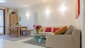 A modern living room with a sofa, a glass coffee table, a dining table with chairs, and a radiator. - CASA SAN GIORGIO, Family Apartment (Solarolo)