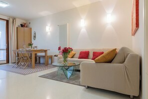 A modern living room with a sofa, a glass coffee table, a dining table with chairs, and a radiator. - CASA SAN GIORGIO, Family Apartment (Solarolo)