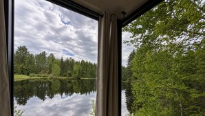 A room with a large window offering a view of a lake surrounded by trees.