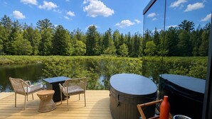 A wooden deck with outdoor furniture, a hot tub, and a view of a lake and forest.