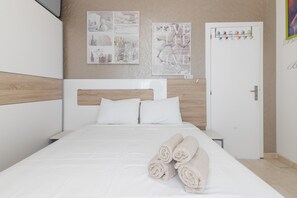 Ein ordentlich bezogenes Bett mit aufgerollten Handtüchern, einem hölzernen Kopfteil und einer weißen Wand mit zwei gerahmten Bildern.