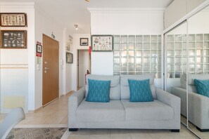 Ein Wohnzimmer mit grauem Sofa, türkisfarbenen Kissen, einer Holztür und einer Wand aus Glasbausteinen.