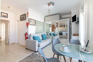 Ein modernes Wohnzimmer mit einer Couch, einem Esstisch, Stühlen und einer Küche im Hintergrund.