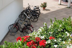 Des vélos appuyés contre un mur, un pot de fleurs et un parterre fleuri.