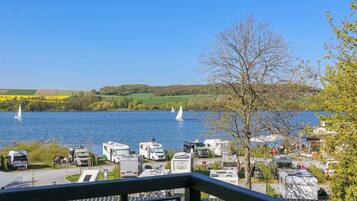 Un terrain de camping pour véhicules récréatifs situé au bord d’un lac, avec plusieurs véhicules stationnés près de l’eau, un ciel dégagé et des voiliers sur le lac.