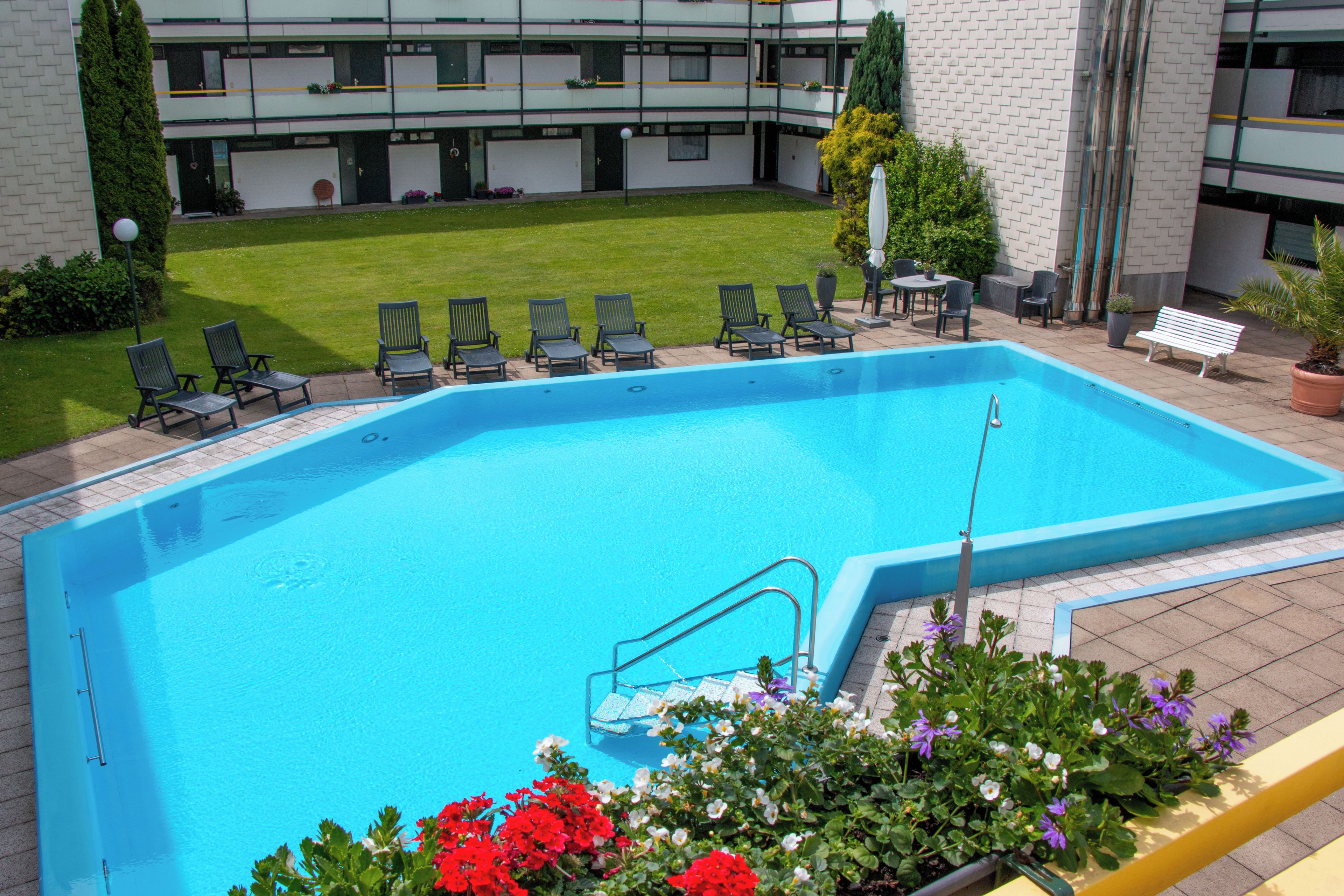 A swimming pool with a metal ladder, surrounded by lounge chairs and a small garden area with flowers.