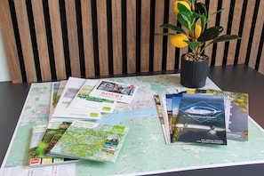 A table with maps and brochures, a potted plant, and a striped wall in the background. - Design-FeWo at the Möhnesee with unique lake view, balcony, pool, sauna, elevator (Möhnesee)