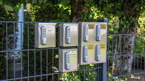 Four keypad security boxes mounted on a metal fence with greenery in the background. - Design-FeWo at the Möhnesee with unique lake view, balcony, pool, sauna, elevator (Möhnesee)