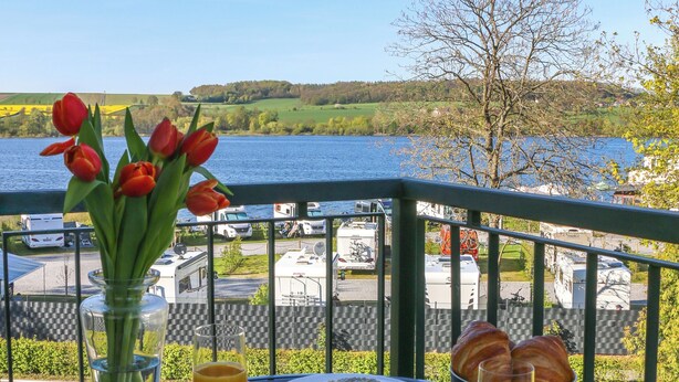 A table with breakfast items and a vase of tulips on a balcony overlooking a lake. - Design-FeWo at the Möhnesee with unique lake view, balcony, pool, sauna, elevator (Möhnesee)