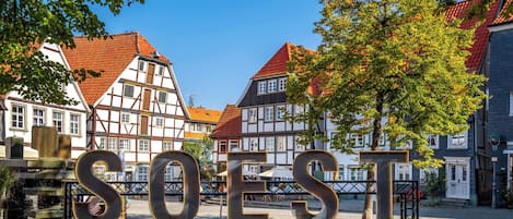 Ett historiskt torg med traditionella hus som har fasader av trä och sten, och en stor, upplyst skylt som visar ordet ”SOEST”.