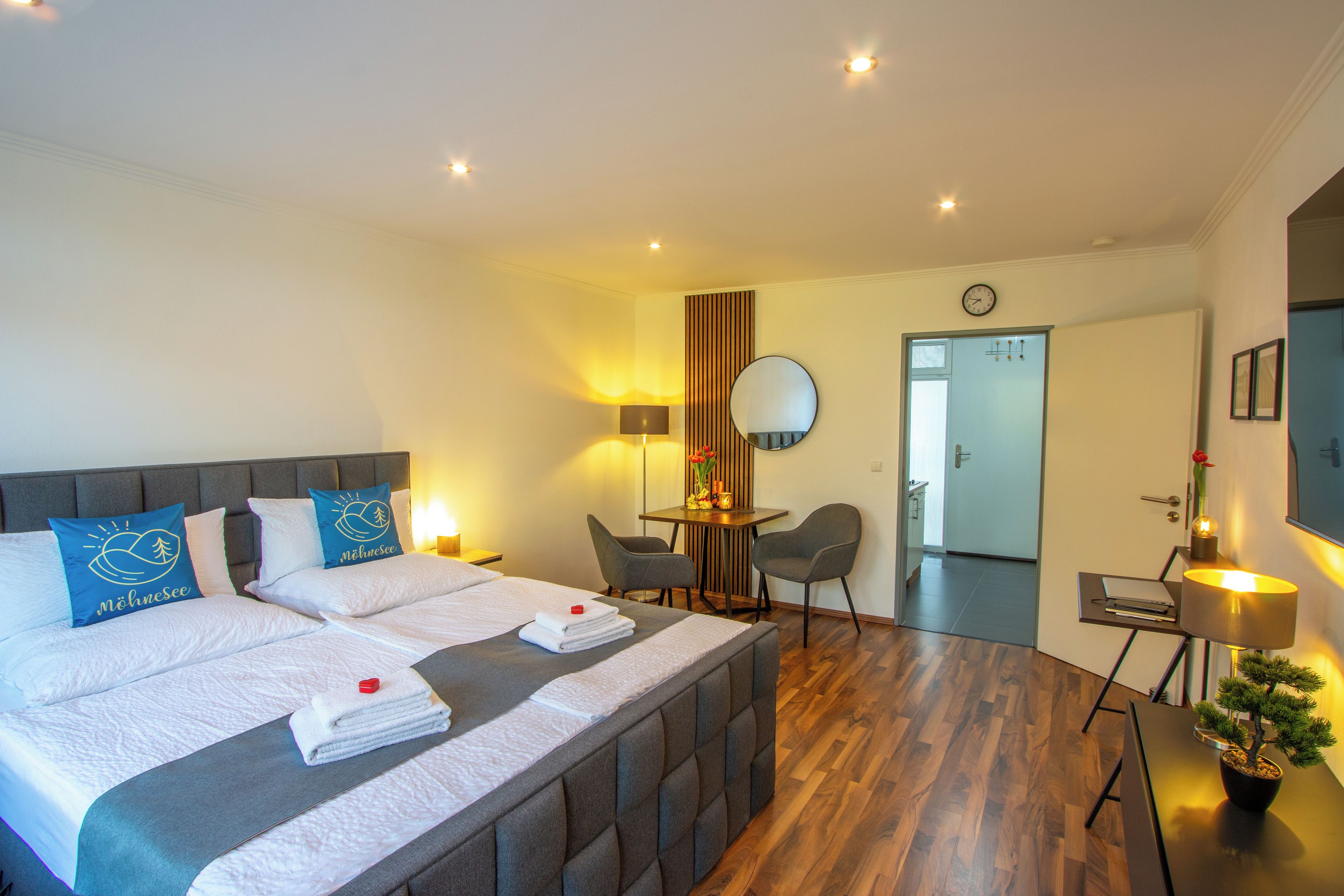 Een hotelkamer met een bed, nachtkastjes, een bureau, een stoel, een spiegel, een klok en een potplant.