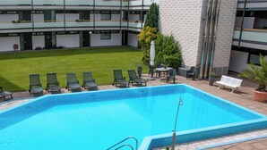 A swimming pool with lounge chairs and a bench, surrounded by a well-maintained lawn and a building with multiple floors and balconies. - Design-FeWo at the Möhnesee with unique lake view, balcony, pool, sauna, elevator (Möhnesee)