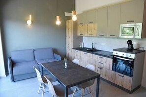 A modern kitchen with wooden cabinets, a built-in oven, and a dining area with a table and chairs. - Mamì cottage: accommodation Bisalta (Grassini)