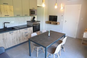 A modern kitchen with wooden cabinets, a built-in microwave, an oven, and a dining area with a table and chairs. - Mamì cottage: accommodation Bisalta (Grassini)