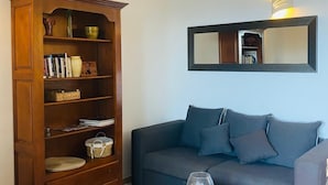 A living room with a dark blue sofa, a wooden bookcase, and a small wooden coffee table with a glass vase. - RESIDENCE PINARELLO CORSE SUD, MINI VILLA, SEA AND BEACH VIEW ON FOOT, for 6 (Zonza)
