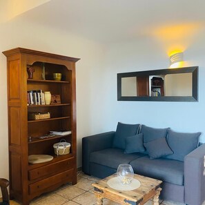 Ein Wohnzimmer mit einem dunkelblauen Sofa, einer Holzbibliothek und einem kleinen Holztisch mit einer Glasvase.