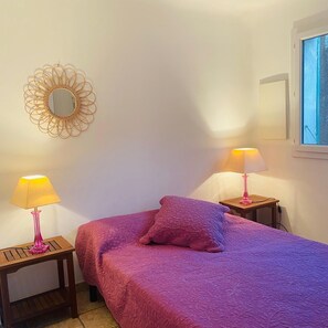 Ein Schlafzimmer mit einem Bett, zwei Nachttischen mit Lampen, einem Zier-Spiegel und einem Fenster.