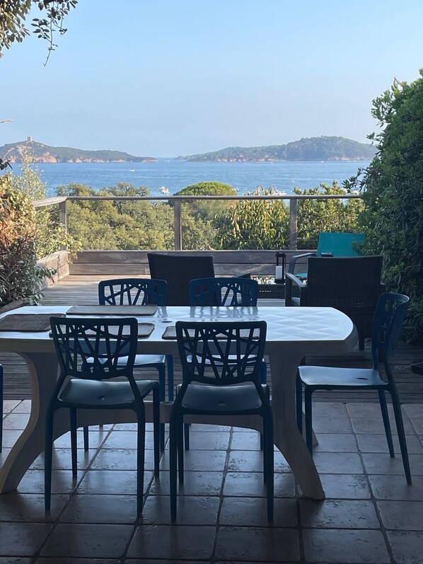 Une terrasse extérieure avec une table et des chaises, une vue sur la mer et un paysage montagneux en arrière-plan.