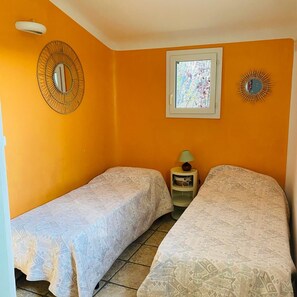 Ein Zimmer mit zwei Betten, einem Fenster, einem Spiegel und einer Lampe auf einem Nachttisch.