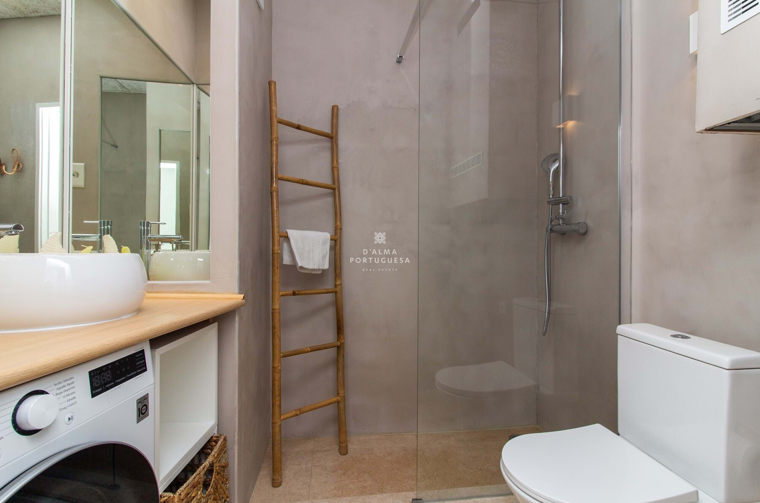 A modern bathroom with a glass shower enclosure, a wooden ladder, a washing machine, and a toilet.