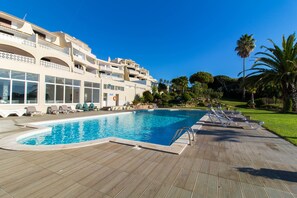 Ein Pool mit Liegestühlen, ein Gebäude mit Balkonen und Palmen.