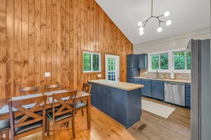 Eine moderne Küche mit Holzwänden, einer zentralen Kochinsel und einem Essbereich mit Holzstühlen.