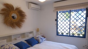Una camera da letto con un letto, un condizionatore d'aria a parete, una finestra con inferriate e uno specchio decorativo.