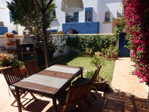 Eine Terrasse im Freien mit Holztisch und -stühlen, umgeben von Blumentöpfen und einem kleinen Garten.